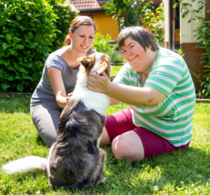 Two smiling women sitting on the grass petting a dog