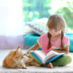 Little girl reading to an orange cat